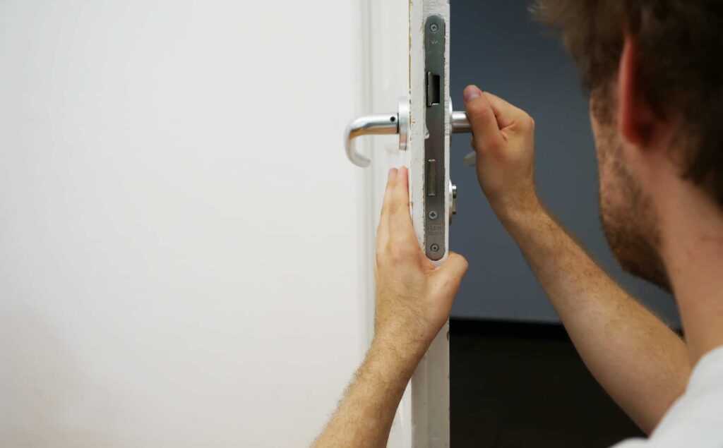 locksmith tech holding a handle of a commercial lock on a door for changing it and rekey it
