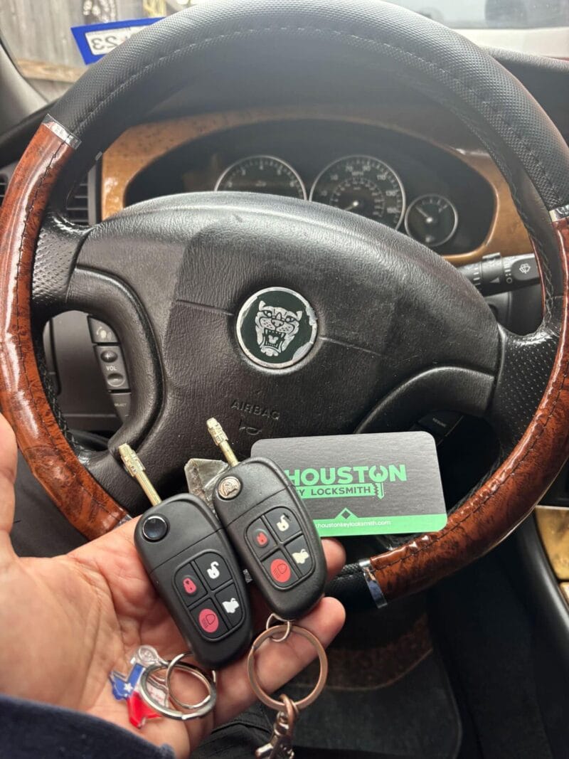 A professional locksmith holding a programmed car key fob and remote in front of a Jaguar steering wheel.
