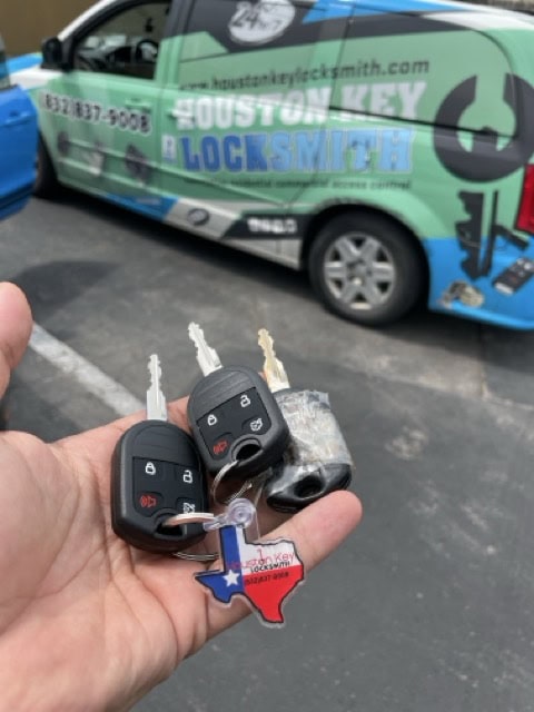 Hand holding replacement car keys in front of a locksmith service van in Midtown Houston.