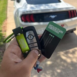 A locksmith holding a newly programmed car key fob in front of a white vehicle, demonstrating how a locksmith can make akey without the original